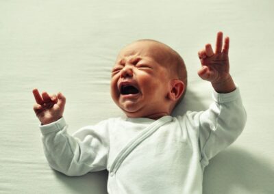 A baby is laying on a bed with his hands up, experiencing body stress.