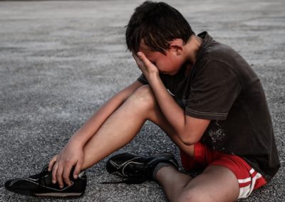 A young boy experiencing Body Stress Release while sitting on the ground with his hand on his head.
